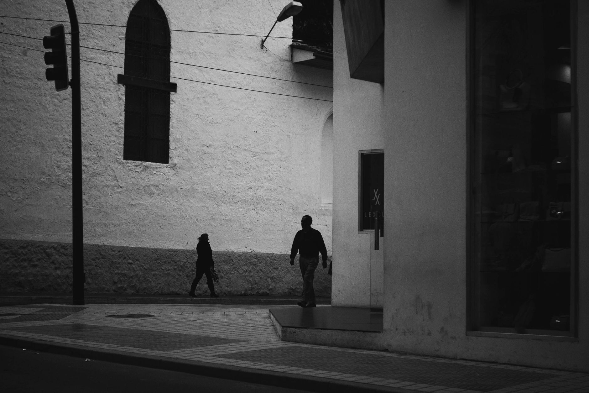 Deux passants en silhouette marchent le long d’un mur clair, scène de rue en noir et blanc