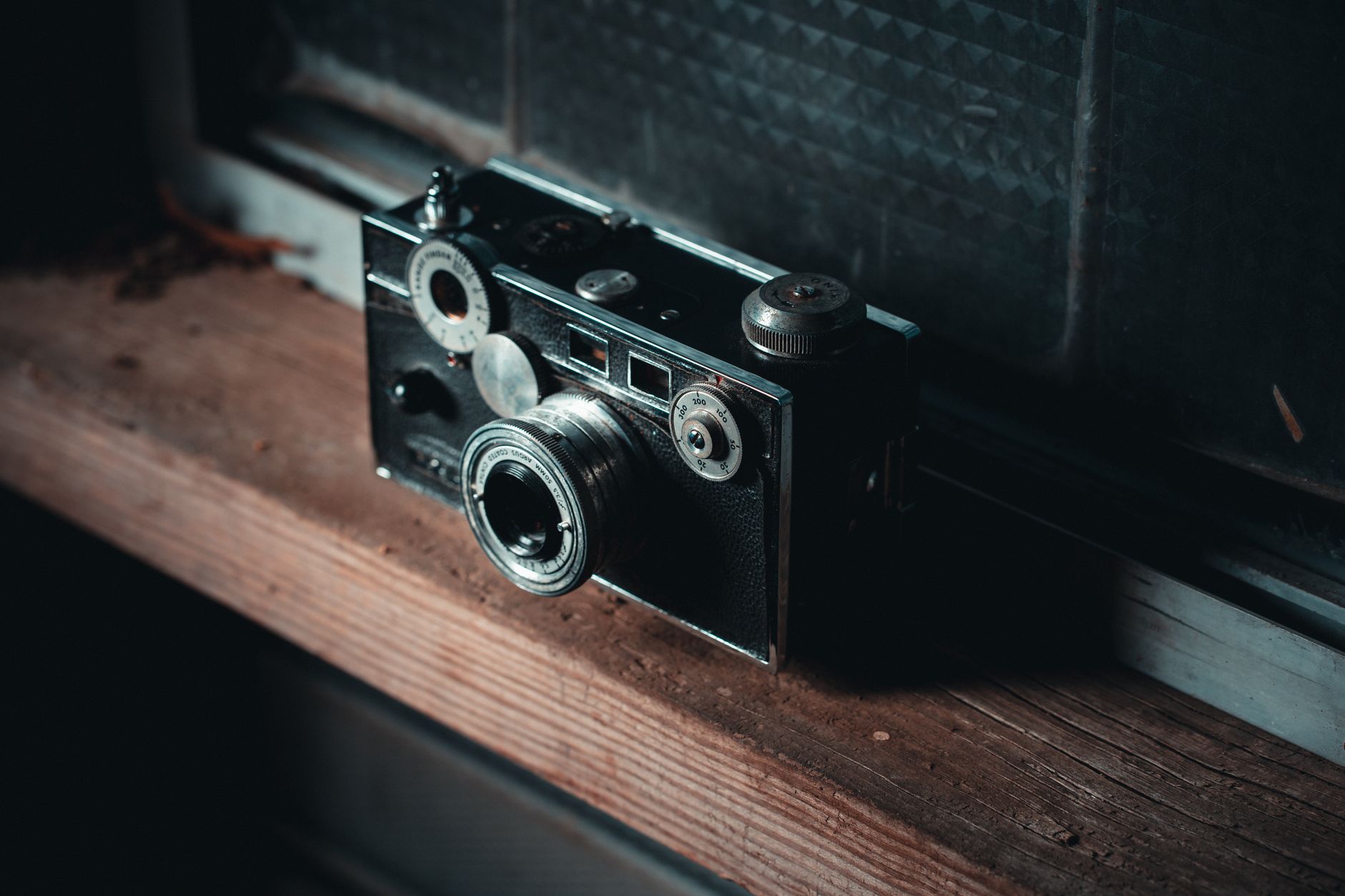 Un ancien boîtier photographique argentique en métal et cuir posé sur un rebord en bois.